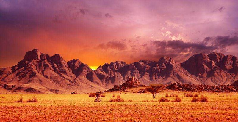 10 Destinazioni Esotiche da Esplorare nel 2023, dalle steppe asiatiche 4 Majestic mountain landscape at sunset in desert region, vibrant sky with pink and purple hues, arid terrain with sparse vegetation, perfect for travel and nature photography.