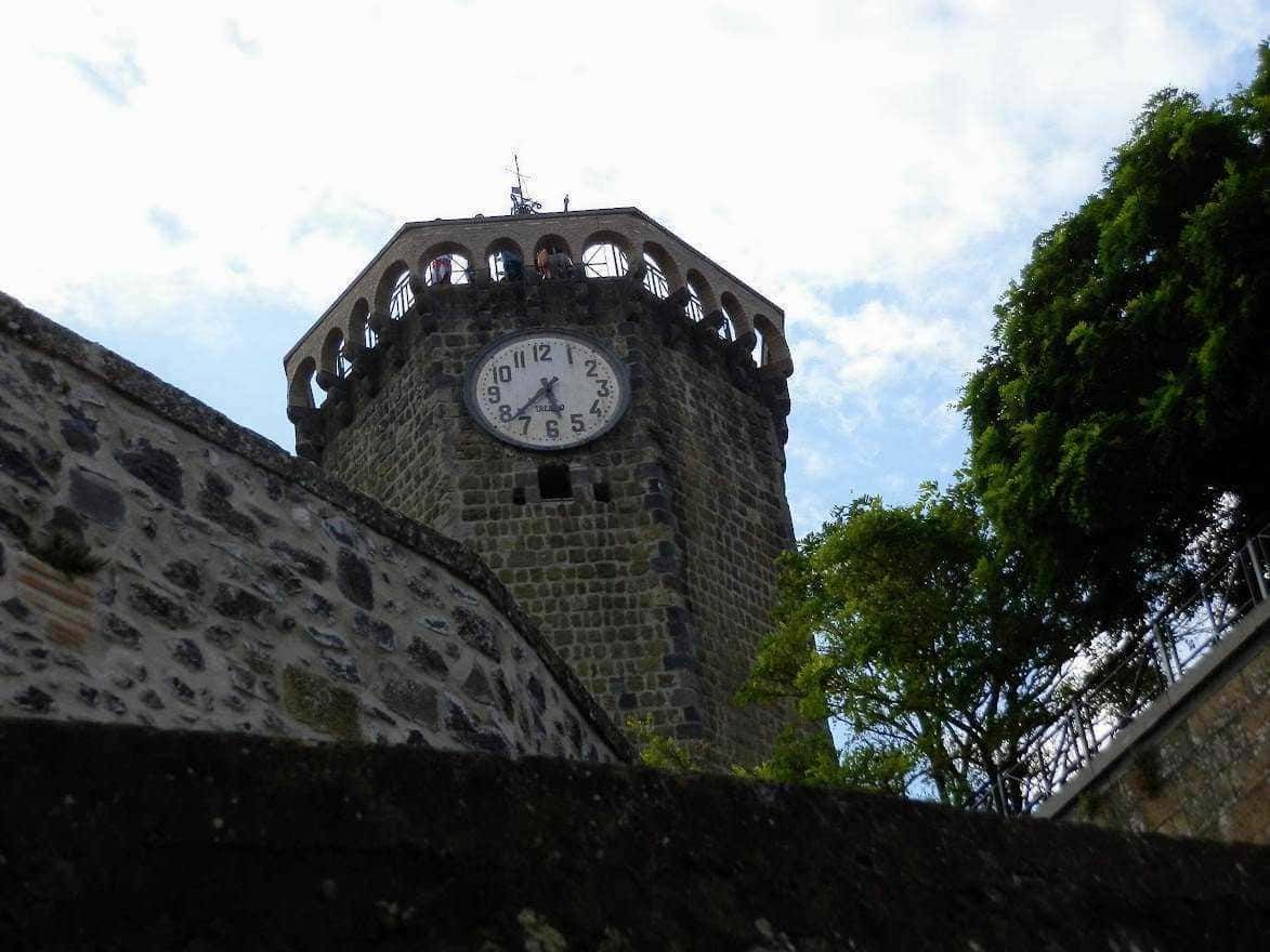 Campanile storico con orologio, vista dall'angolo, circondato da alberi e cielo nuvoloso, esempio di architettura medievale, simbolo di un centro cittadino italiano.