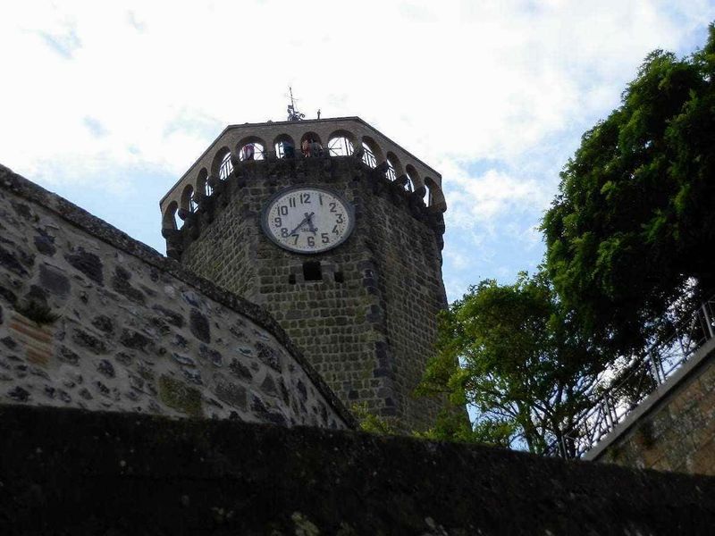 11 Borghi e luoghi da visitare nel Lazio Nord-Ovest 14 Campanile storico con orologio, vista dall'angolo, circondato da alberi e cielo nuvoloso, esempio di architettura medievale, simbolo di un centro cittadino italiano.