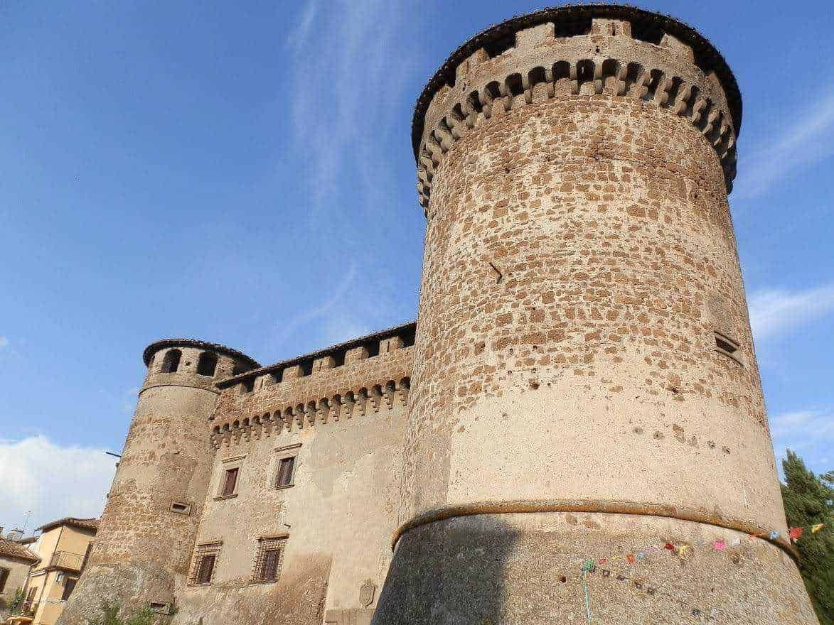 Antica torre difensiva in pietra con merlature, parte di un castello storico, sotto un cielo azzurro con nuvole sparse. Ideale per articoli su storia, architettura medievale e turismo culturale.