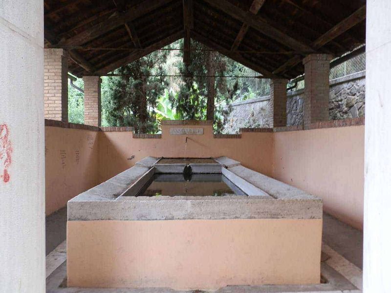 11 Borghi e luoghi da visitare nel Lazio Nord-Ovest 10 Lavatório storico all'aperto sotto un tetto di legno, circondato da pareti in pietra e mattoni, immerso nel verde, ideale per relax e socializzazione all'aperto.