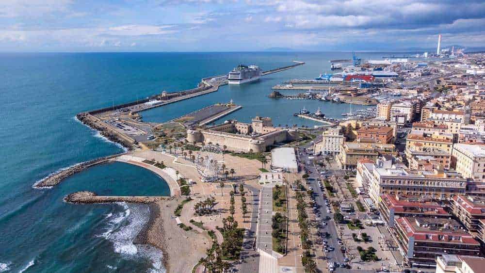 Vista panoramica del porto di Cagliari con imbarcazioni, strutture portuali e il mare durante una giornata soleggiata.
