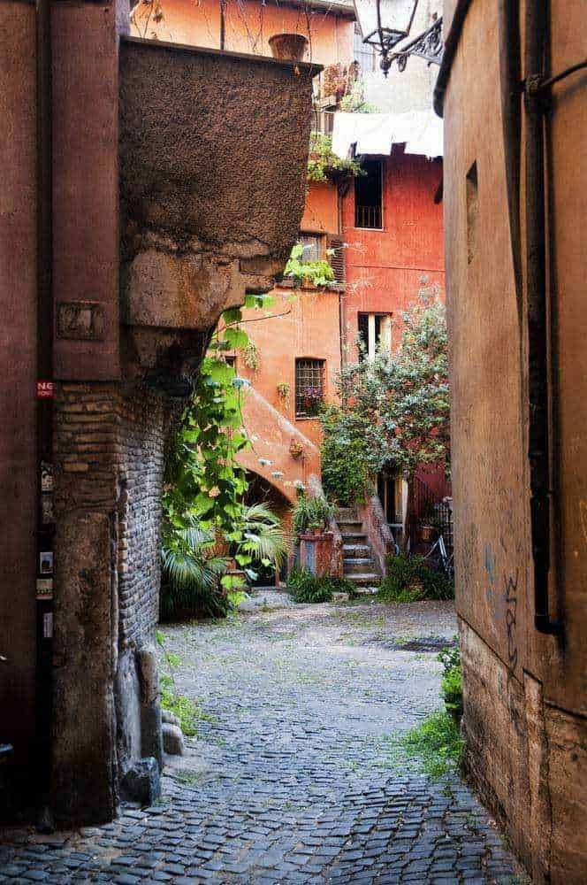 Vecchio vicolo romano con edifici color terracotta, piante verdi e scalinate in pietra, atmosfera suggestiva e tranquilla, ideale per appunti sul blog su viaggi e lifestyle italiani.