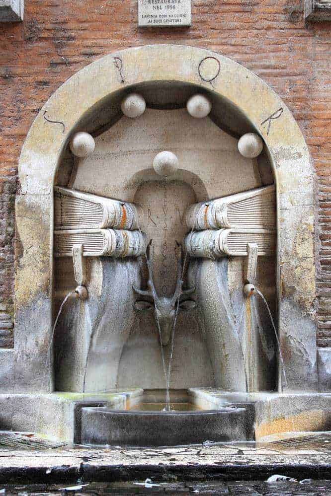 22 rioni storici di Roma: cose da vedere, nomi e storia 5 Pompa dell'acqua storica di una fontana di pietra, con tubi in ottone e acqua che sgorga, situata in un contesto urbano antico.