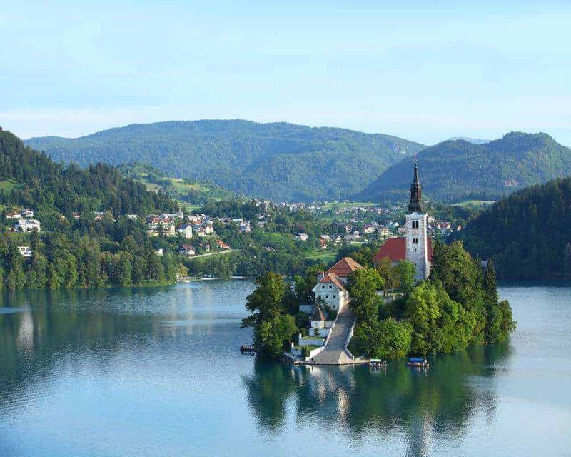8 Città lacustri per vacanze al lago in Europa 3 Isola con chiesa e campanile situata su un lago tra le montagne verdi, creando un paesaggio pittoresco e tranquillo, ideale per foto panoramiche e turismo naturalistico.