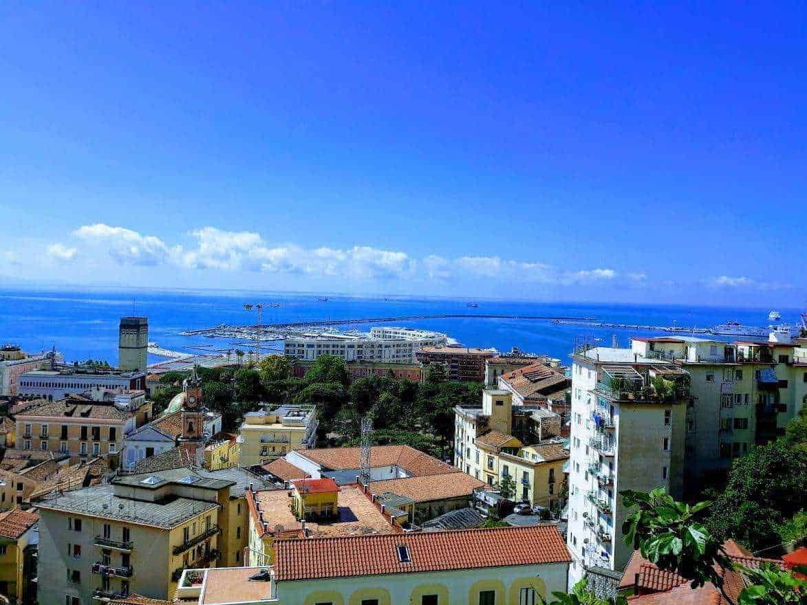 Vista panoramica del porto di Messina e del golfo, con cielo sereno e edifici storici lungo la costa siciliana. Un'immagine che rappresenta l'architettura mediterranea e il panorama marittimo.