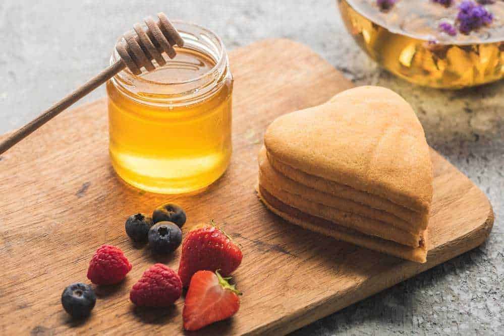 Miele, crepes a forma di cuore, frutti di bosco freschi su un tagliere in legno. Colazione sana e gustosa con dolci e miele naturale. Ottima idea per una colazione romantica o un brunch estivo.