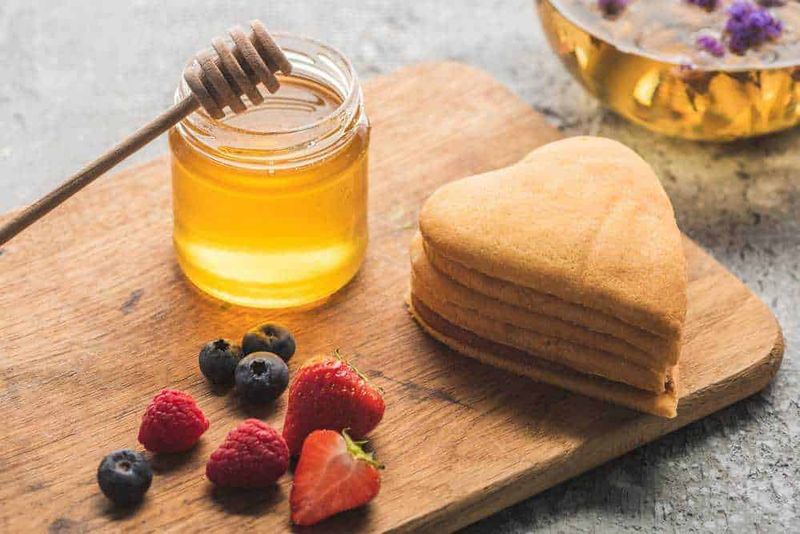 Miele e dieta: come inserirlo e usarlo al posto dello zucchero 3 Miele, crepes a forma di cuore, frutti di bosco freschi su un tagliere in legno. Colazione sana e gustosa con dolci e miele naturale. Ottima idea per una colazione romantica o un brunch estivo.