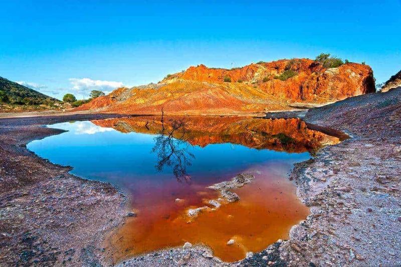 10 Attrazioni Isola d'Elba in 2 ore 4 Paesaggio naturale con lago riflettente, colline rosse e cielo blu, ideale per appunti sul blog dedicati all'ambiente e alla natura.