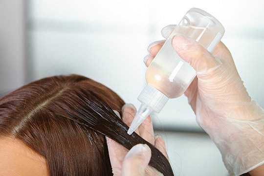 Applicazione di trattamento colorante sui capelli con precisione e guanti di protezione, per un colore professionale e duraturo.