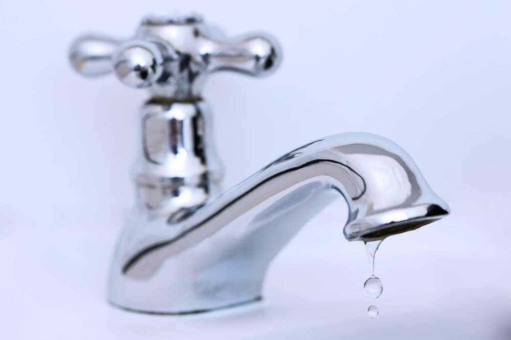 Flessa d'acqua che gocciola da un rubinetto in metallo cromato, simbolo di risparmio idrico e manutenzione domestica. Perfetto per articoli sul risparmio acqua e consigli per la casa.