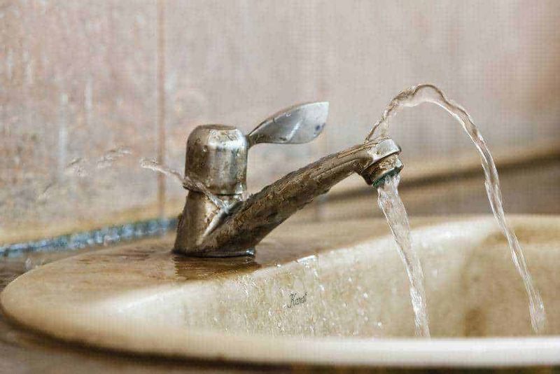 Rubinetto dell'acqua che scorre su un lavabo in pietra, ambiente domestico, dettaglio di un lavandino antico, atmosfera calda e accogliente, stile rustico.