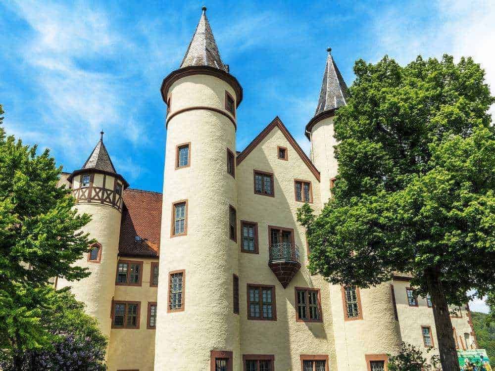 Castello fiabesco con torri alte e pareti in pietra, immerso in un parco verdeggiante, atmosfera da favola medievale, ideale per visite turistiche e appassionati di storia e architettura.