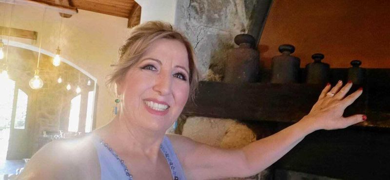 Come mantenere una pelle giovane e fresca con le creme giorno? 5 Appunti Sul Blog, immagine di una donna sorridente che si appoggia a una pietra nel soggiorno di una casa rustica con camino, atmosfera calda e accogliente.