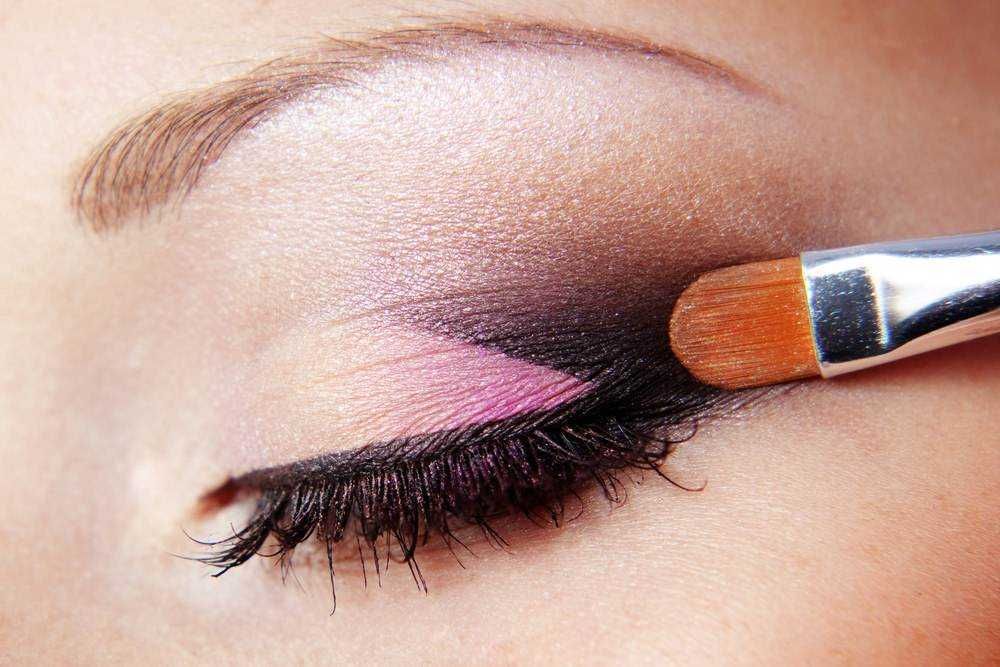 Pennello per trucco occhi che applica ombretto rosa e nero, primo piano su dettaglio di make-up occhi.
