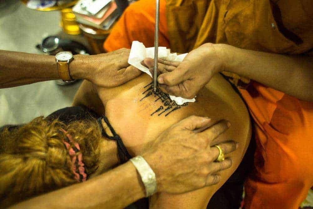 Penna e inchiostro sulla pelle per tatuaggi culturali tradizionali asiatici, evidenziando l'arte del tatuaggio tradizionale in un contesto sociale.