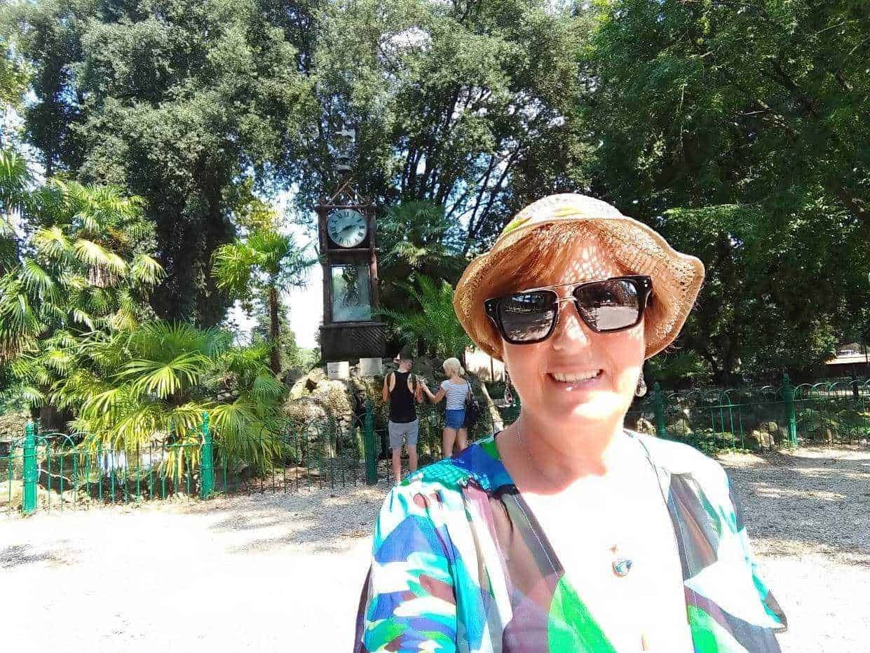 Vita all'aperto con donna sorridente in estate, cappello di paglia e occhiali da sole, in un parco alberato.