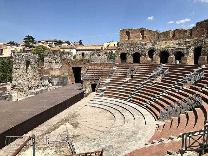 Antico teatro romano all'aperto con sedili in pietra, resti archeologici e ambientazione storica in un sito turistico in Italia.