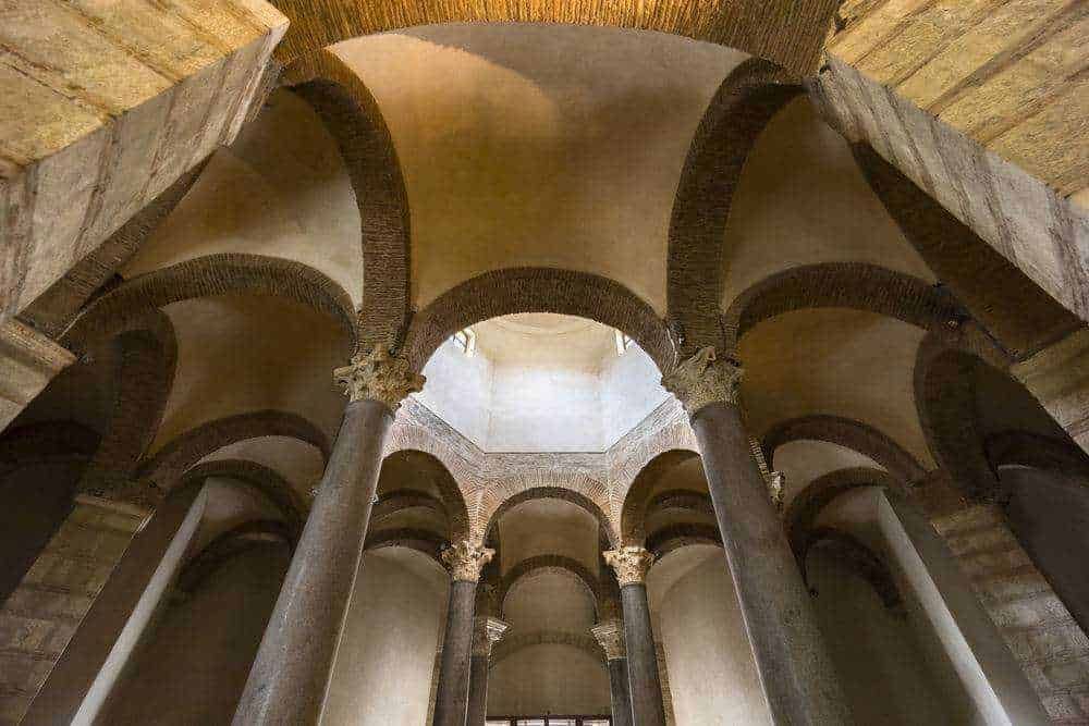 Antico interno di una chiesa con colonne in pietra e archi a tutto sesto, illuminata da luce naturale, esempio di architettura romanica, ambiente spirituale e storico.