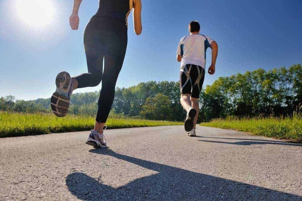 Allenamento di corsa all'aperto, donne e uomini che fanno jogging su strada in un parco con cielo soleggiato, tema benessere e fitness.