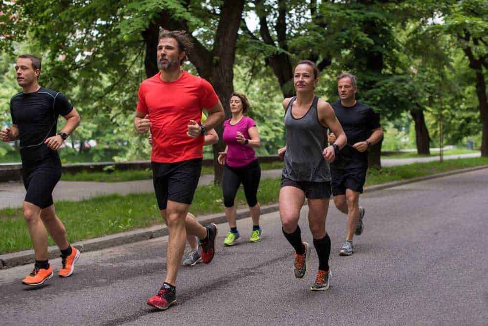 Allenamento di corsa all'aperto in parco con un gruppo di persone che praticano jogging per migliorare salute e benessere. Gruppo di runners che si allenano durante una passeggiata in natura.