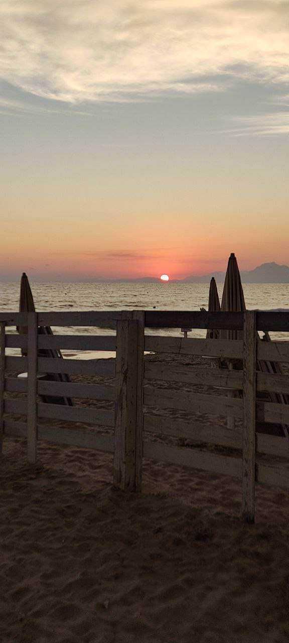 Tramonto sulla spiaggia con ombrelloni e rete in legno, atmosfera tranquilla e rilassante, perfetta per vacanze estive, lontano dal caos urbano.