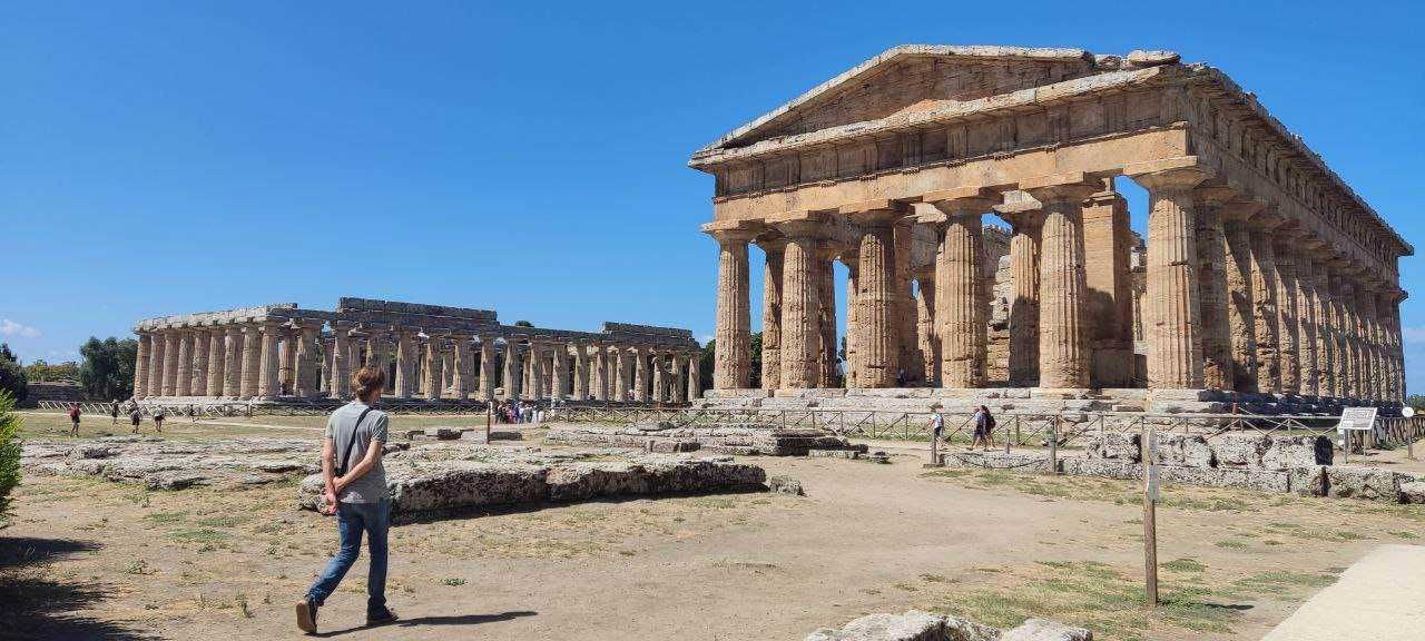 Maestoso tempio greco antico con colonne doriche, sito archeologico in Grecia, visitatori scoprono la storia dell'antica civiltà, cielo azzurro e sole splendente illuminano le rovine.