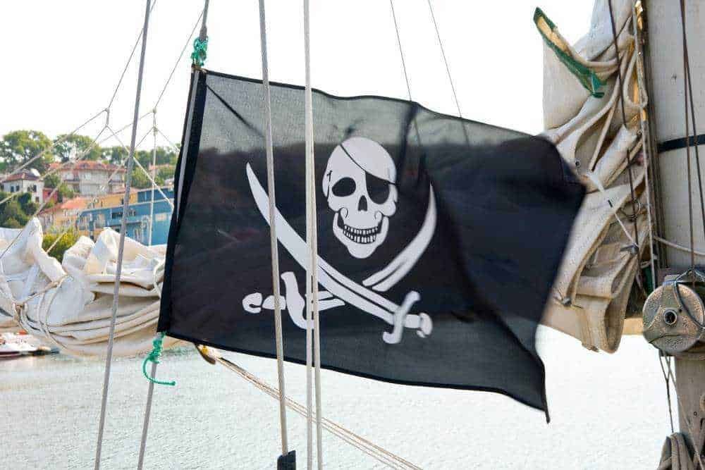 Bandiera pirata con teschio e spada su barca a vela in porto, simbolo di avventura e navigazione, ideale per contenuti su viaggi, nautica e pirateria.