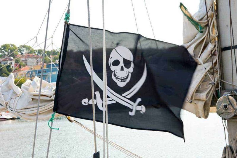 I Cavalieri Templari storia 10 fatti mitici 8 Bandiera pirata con teschio e spada su barca a vela in porto, simbolo di avventura e navigazione, ideale per contenuti su viaggi, nautica e pirateria.
