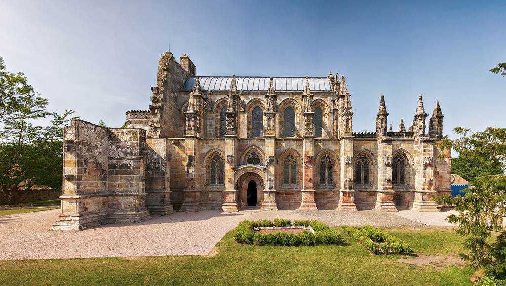 Antica chiesa gotica in pietra, esempio di architettura storica e religiosa, immersa in un parco verde con un cielo sereno. Perfetta per appunti su storia e arte medievale.