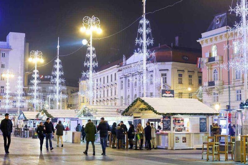 Luoghi di festa natalizia con luminarie, mercatini e persone che godono dell'atmosfera di Natale in una piazza cittadina.
