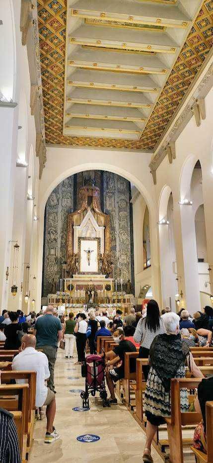 Elegante chiesa cattolica con architettura impressionante, illuminata da luci soffuse, piena di fedeli durante una funzione religiosa, con altare decorato e affreschi sul soffitto.