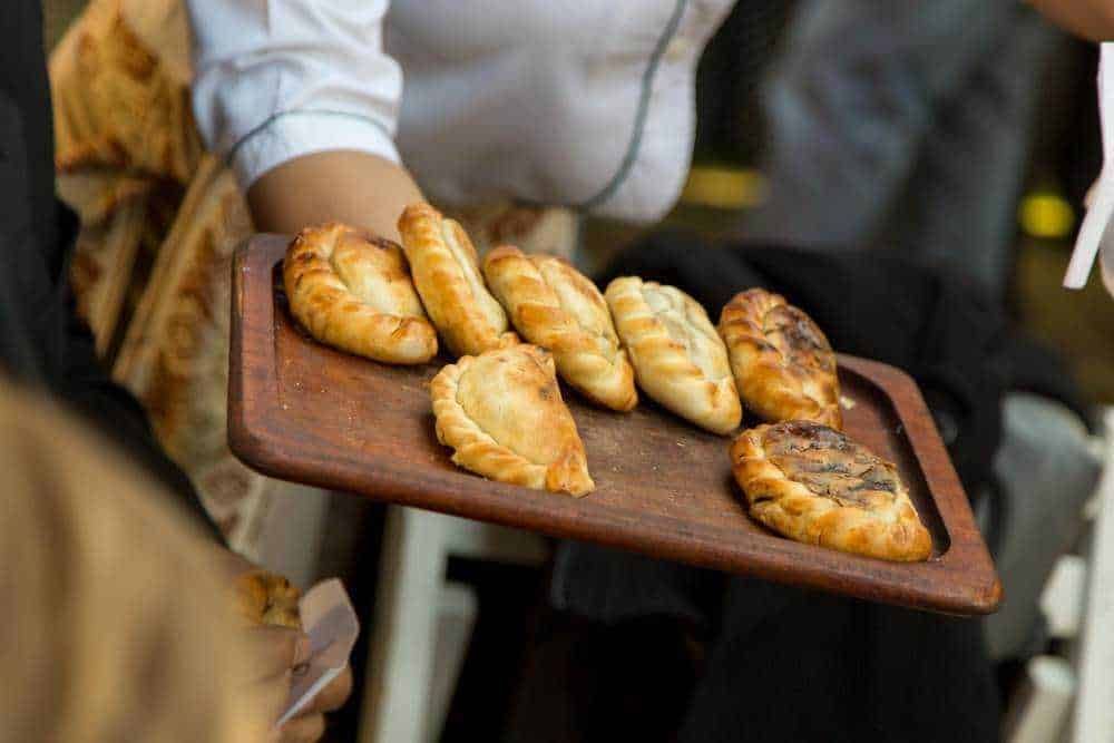 Delicious Italian meat-filled pastries on wooden tray, street food in Italy, traditional calzones and panzerotti, freshly baked savory pies, appetizing snack from food truck.