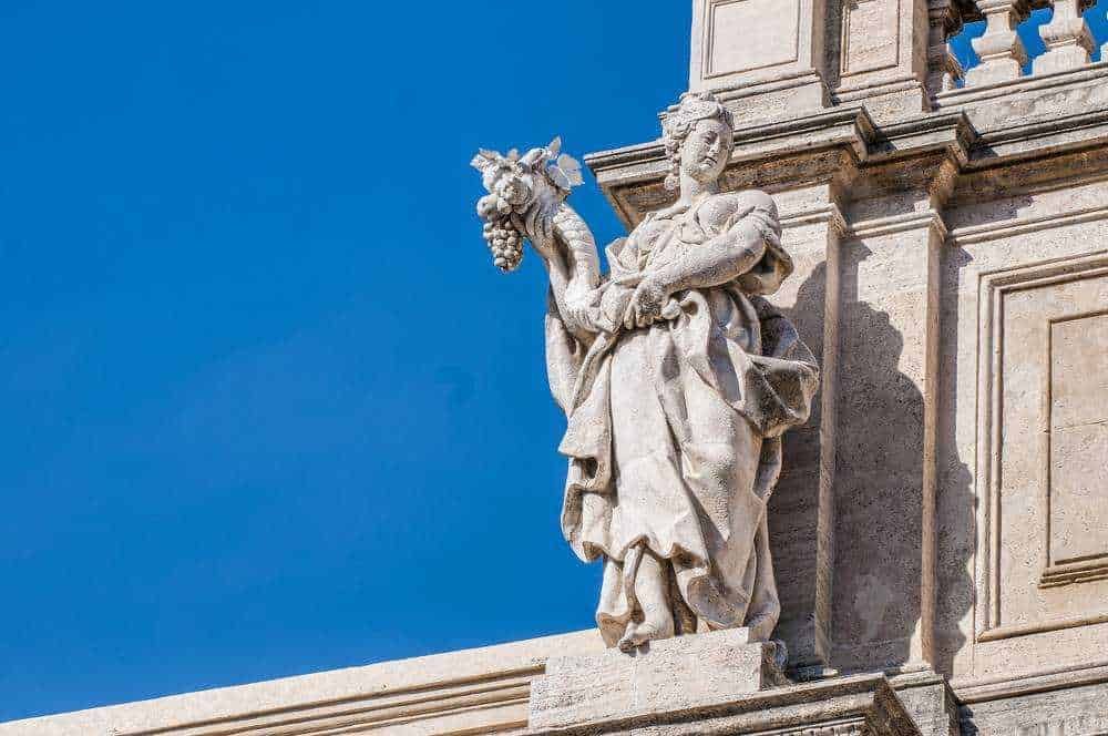 Statua di una donna con grappolo d'uva in pietra sull'architettura storica, simbolo di cultura e arte italiana. Aperto il blog Appunti Sul Blog dedicato a approfondimenti storici e culturali.