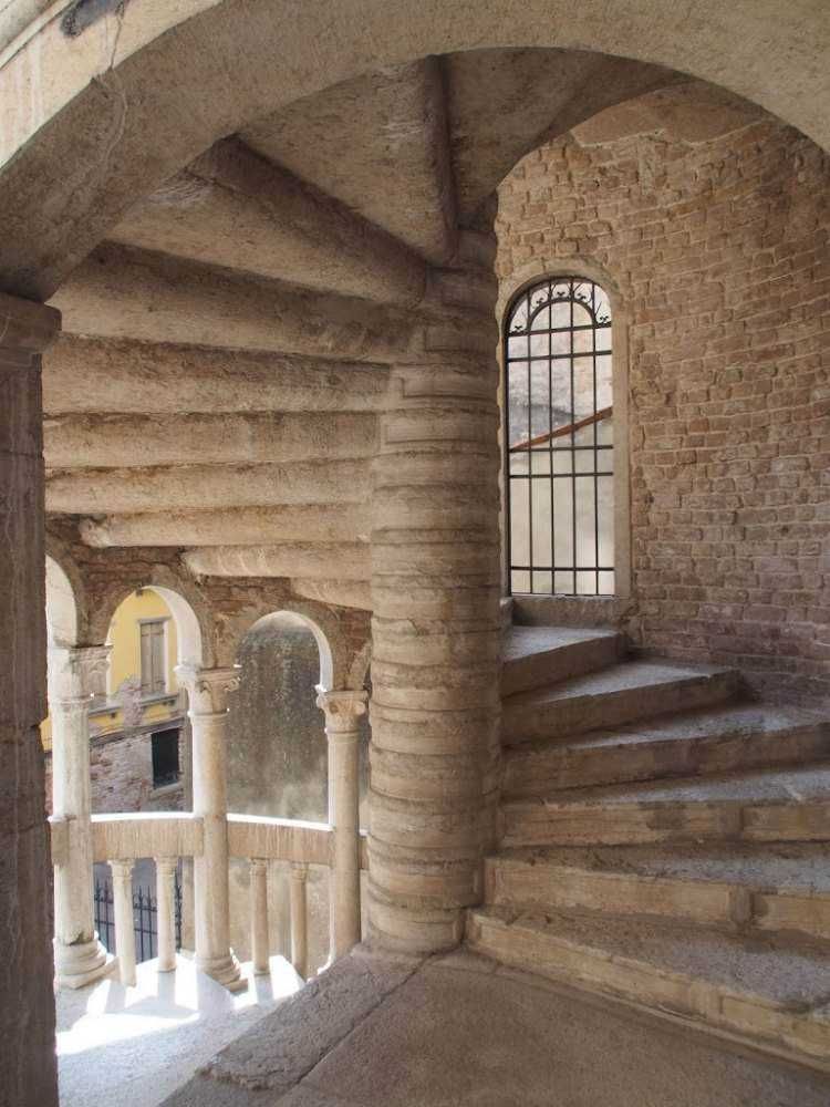 Antica scala in pietra con ringhiera in ferro battuto e vista su un cortile storico di un edificio in stile rinascimentale.