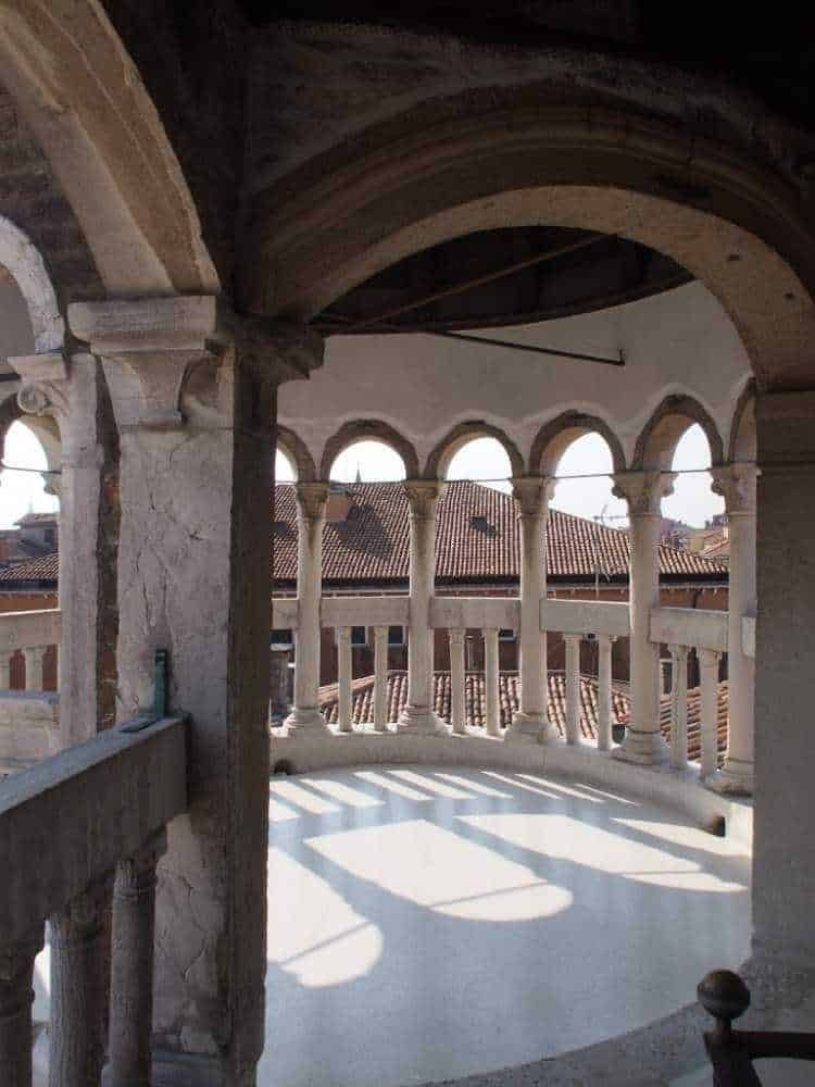 Antico balcone con colonne e archi, vista sui tetti del centro storico, stile architettonico medievale, dettaglio di pietra e legno, atmosfera storica e affascinante.