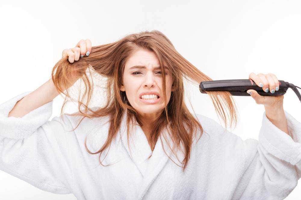 Brava donna arrabbiata che si piastra i capelli, frustrata durante la luminosità del giorno. Donna in vestaglia bianca che si appresta a sistemare i capelli con frustrante esperienza di stile.