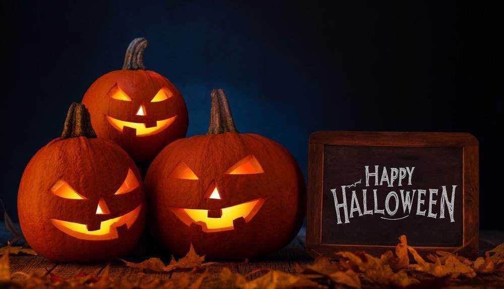 Zucca di Halloween illuminate con sorriso spettrale, decorazioni autunnali con foglie secche e lavagna con scritto "Happy Halloween" in stile festoso, atmosfera misteriosa e festiva.