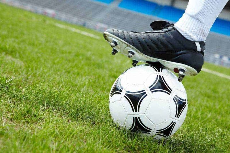 Scegliere le scarpe per 10 tipi di sport 7 Calcio, giocatore con scarpa da calcio che si appoggia su una palla da calcio su un campo verde.
