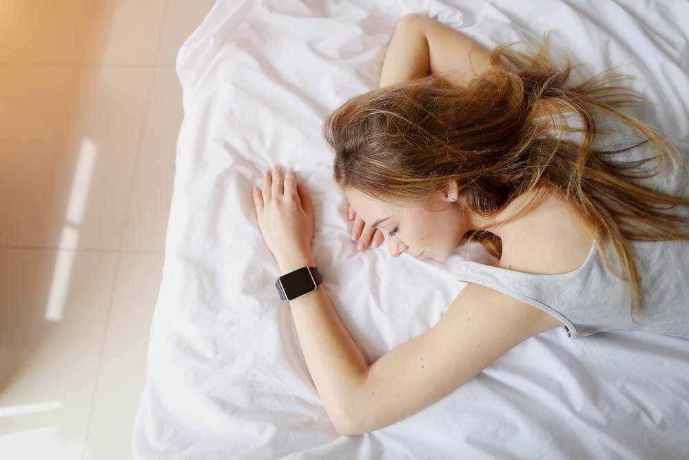 Riposo notte donna con smartwatch distesa su letto, relax, sonno riposante, comfort, stile di vita salutare, benessere mentale, tecnologia indossabile, routine quotidiana, abitudini sane, salute e benessere.