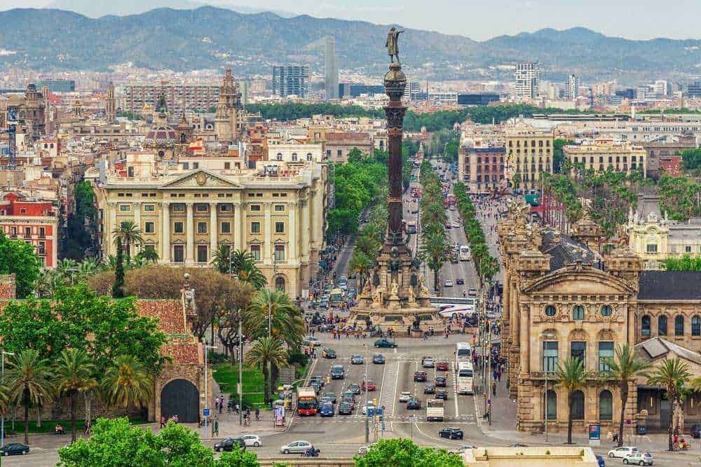 Furgoni in strada a Barcellona con monumento alla Fontana di Canaletes e skyline cittadino sullo sfondo. Panoramica della trafficata arteria principale di Barcellona, Italia.