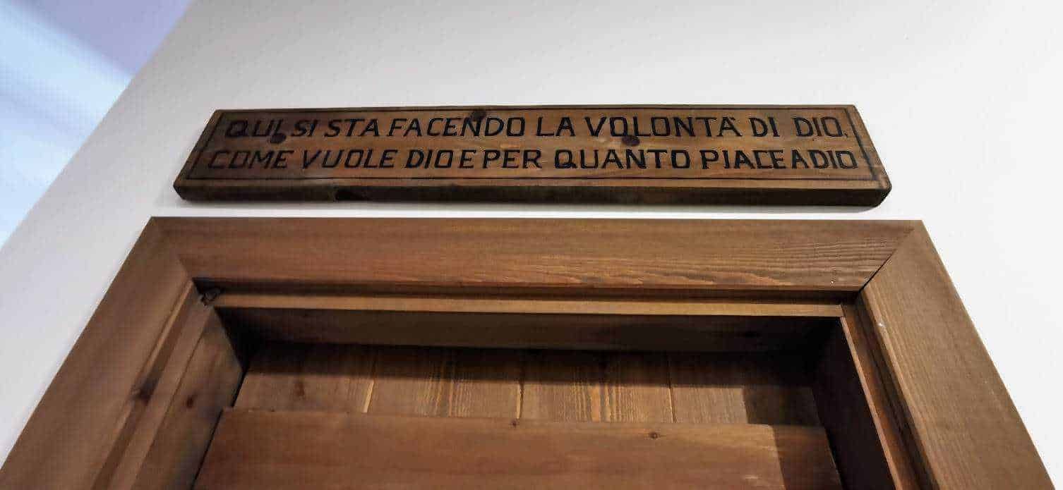 Finestra in legno naturale con cornice, sopra cartello con scrittura religiosa, elemento decorativo e spirituale in ambiente interno, stile minimalista e caldo.