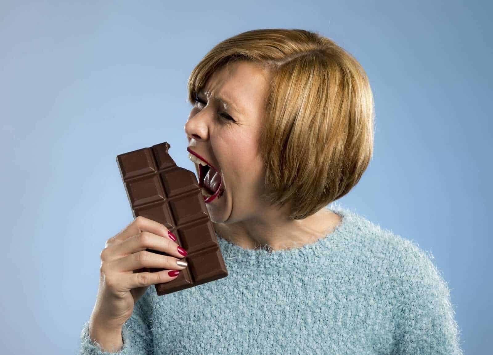 Barretta di cioccolato fondente mangiata da una donna con bocca aperta, emozione di golosità e tentazione, immagine di dolci e cioccolato, perfetta per blog di ricette e lifestyle dolci.