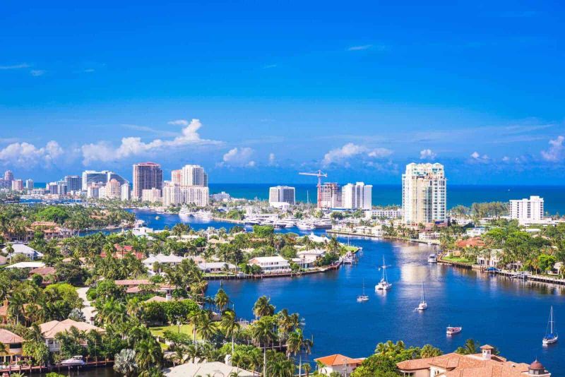 13 Città con canali nel mondo da vedere 12 Vivace skyline di Miami con grattacieli, porto turistico e yacht, immersa in natura tropicale, sotto un cielo azzurro, perfetta combinazione di città moderna e paesaggi marittimi.