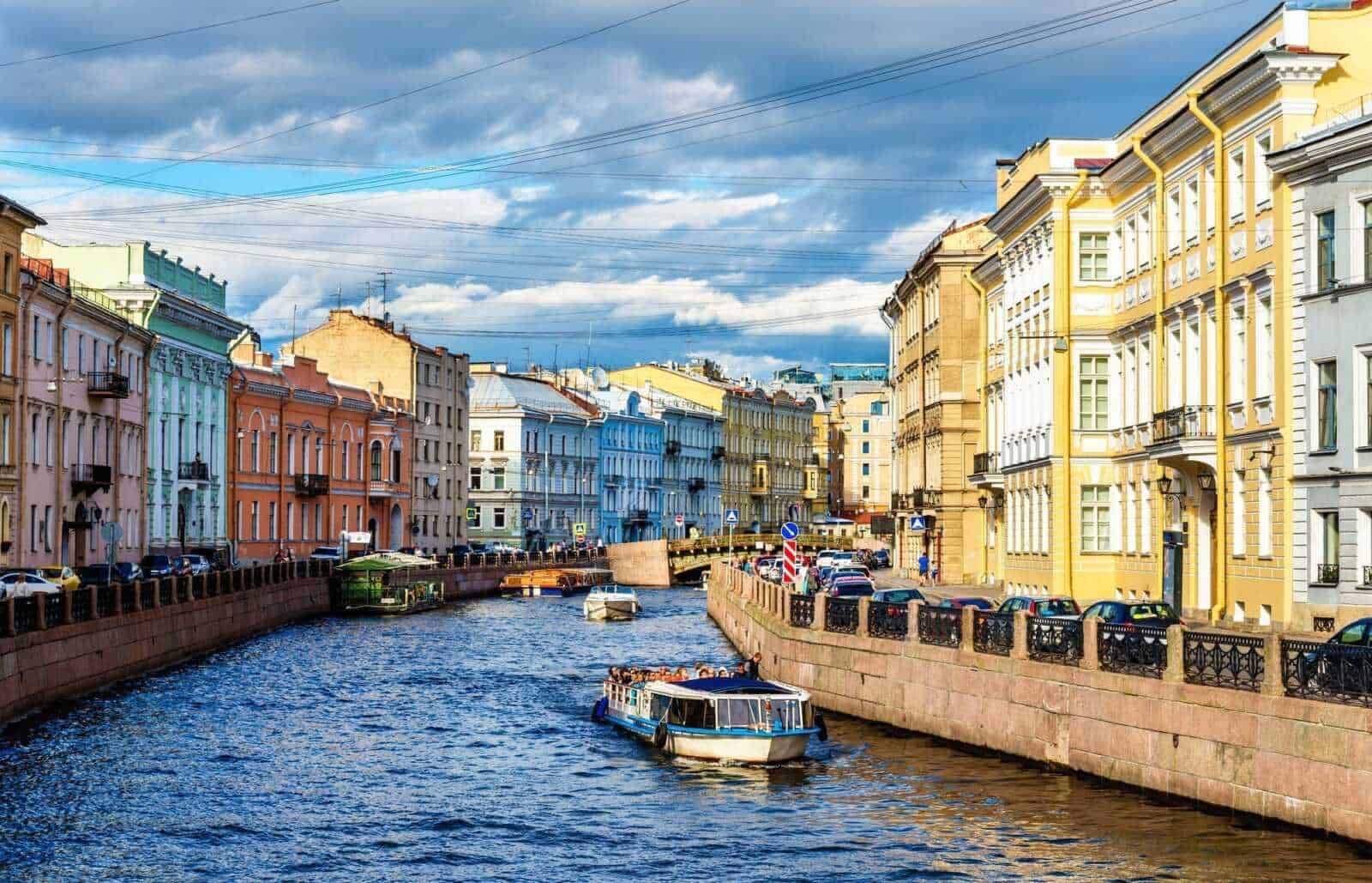 Colorate case storiche lungo il canale di San Pietroburgo, Russia, con barche che navigano sull'acqua sotto un cielo nuvoloso. Edifici colorati e atmosfera vivace in centro città.