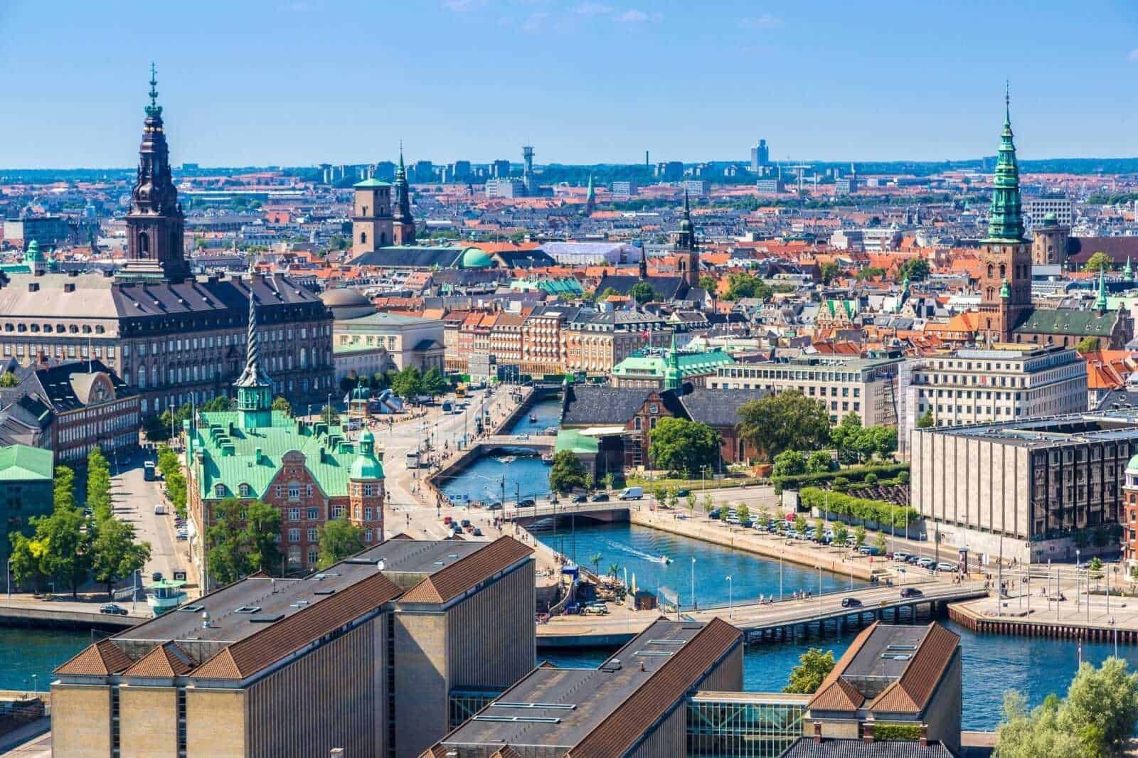 VISTA PANORAMICA DELLA CITTÀ DI COPENHAGEN CON CANALI, TETTI COLORATI E STRUTTURE ARCHITETTONICHE ICONICHE NEL CUORE DANIMARCA, ILLUSTRANDO IL PAESAGGIO URBANO E CULTURALE.