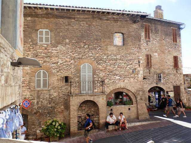 Vecchia casa in pietra con archi e persone che si riposano sulla strada in un borgo italiano storico.