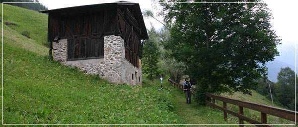 Vecchio chalet in legno con balcone fiorito situato ai piedi di una parete di roccia, immerso nella natura, perfetto per un rifugio montano.