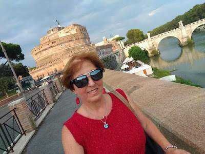 5 mete turistiche in Italia, via libera per un estate in viaggio. Immagine di una donna sorridente con occhiali da sole davanti al Castel Sant'Angelo a Roma, Italia, durante una passeggiata turistica.