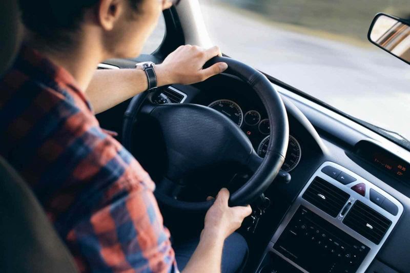 5 trucchi per risparmiare quando si noleggia una macchina 4 Guidatore con camicia a quadri che tiene il volante dell'auto, vista da dietro, durante un viaggio su strada.